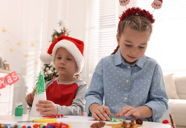 Photo of Cute little children making Christmas crafts at table in decorated room