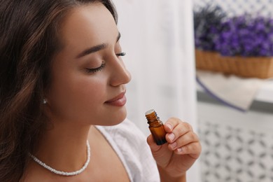 Beautiful young woman with bottle of essential oil indoors