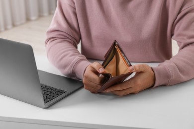 Man with empty wallet at white table indoors, closeup