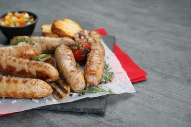Photo of Tasty fresh grilled sausages with vegetables on grey table, closeup. Space for text