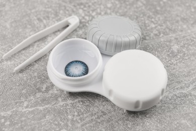 Photo of Case with color contact lenses and tweezers on light grey table, closeup