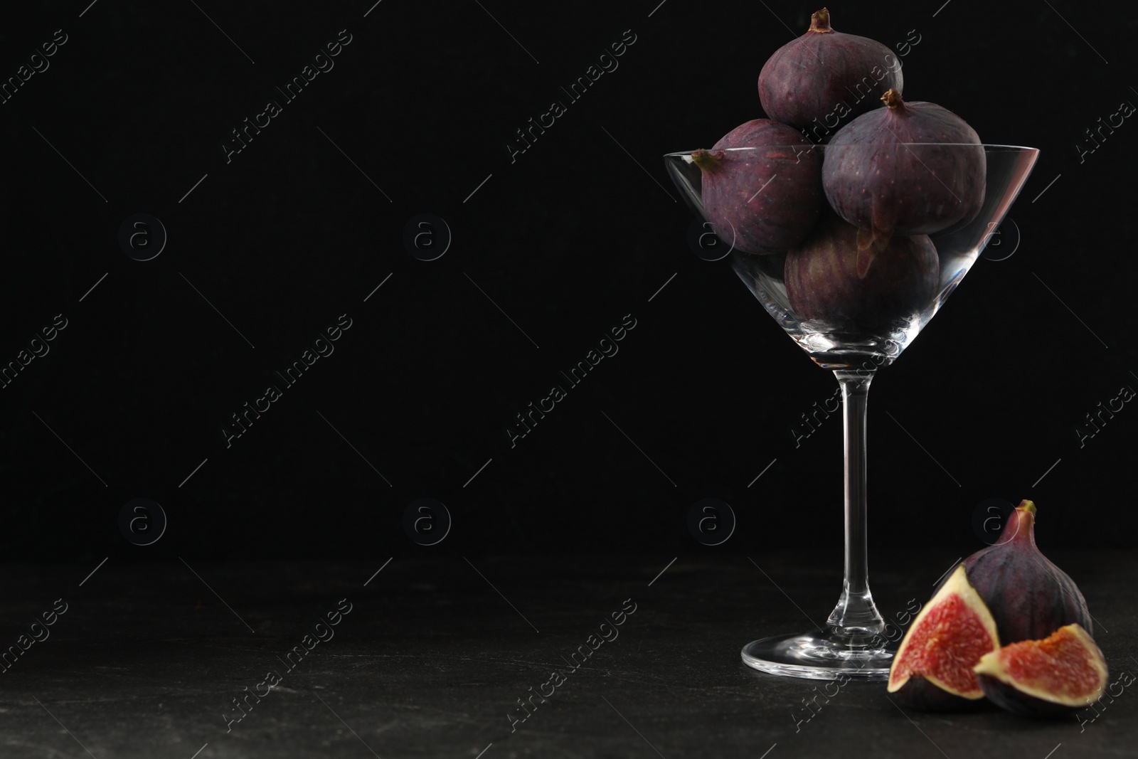 Photo of Tasty raw figs in martini glass on black table. Space for text
