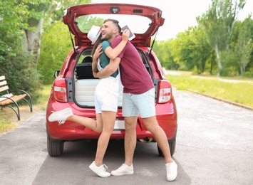 Beautiful young couple near car and suitcase packed for summer journey in trunk