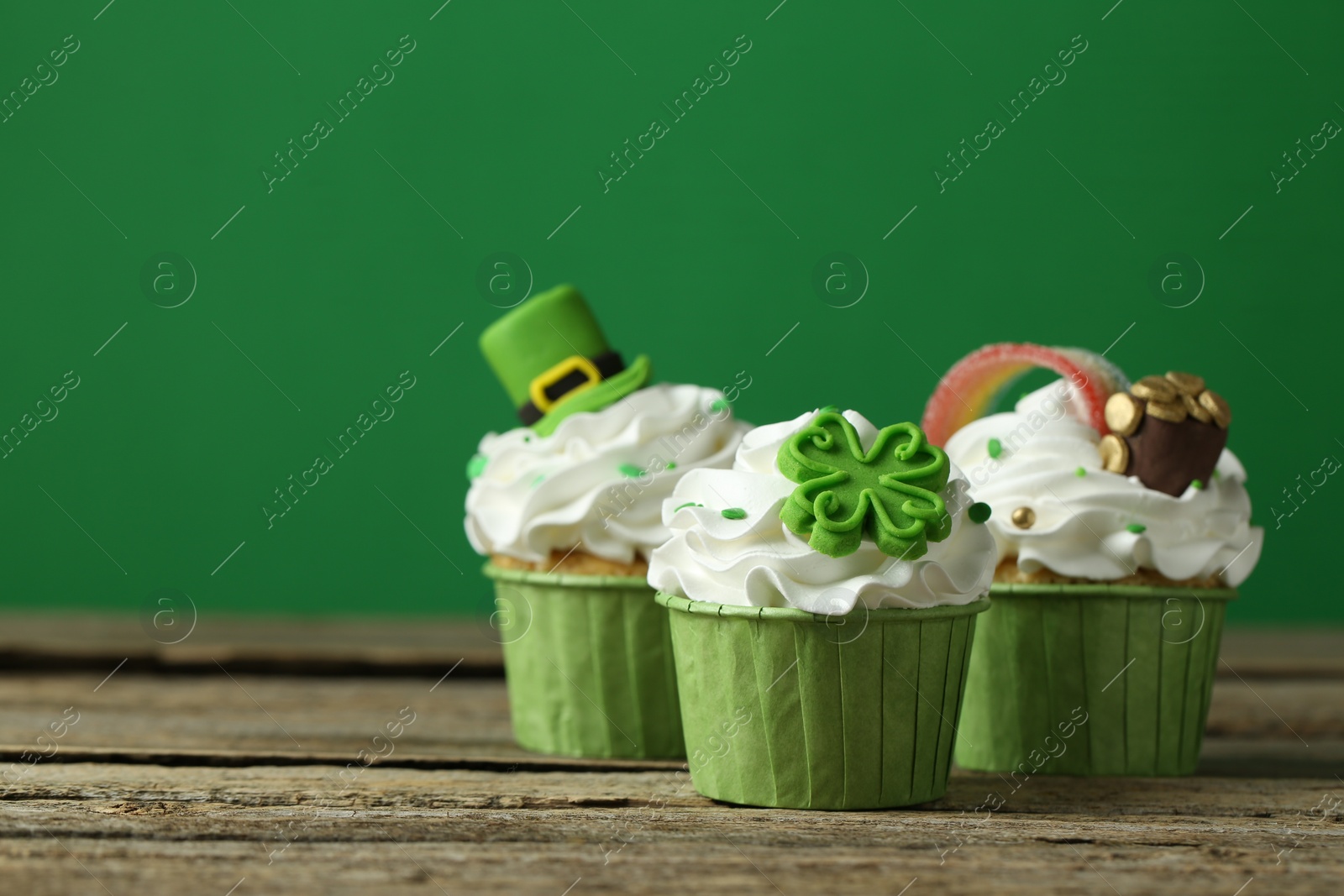 Photo of St. Patrick's day party. Tasty festively decorated cupcakes on wooden table, closeup. Space for text