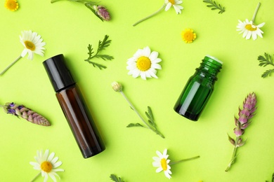 Bottles of different essential oils and wildflowers on color background, flat lay