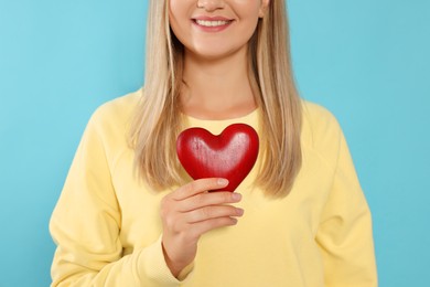 Happy volunteer holding red heart with hands on light blue background, closeup