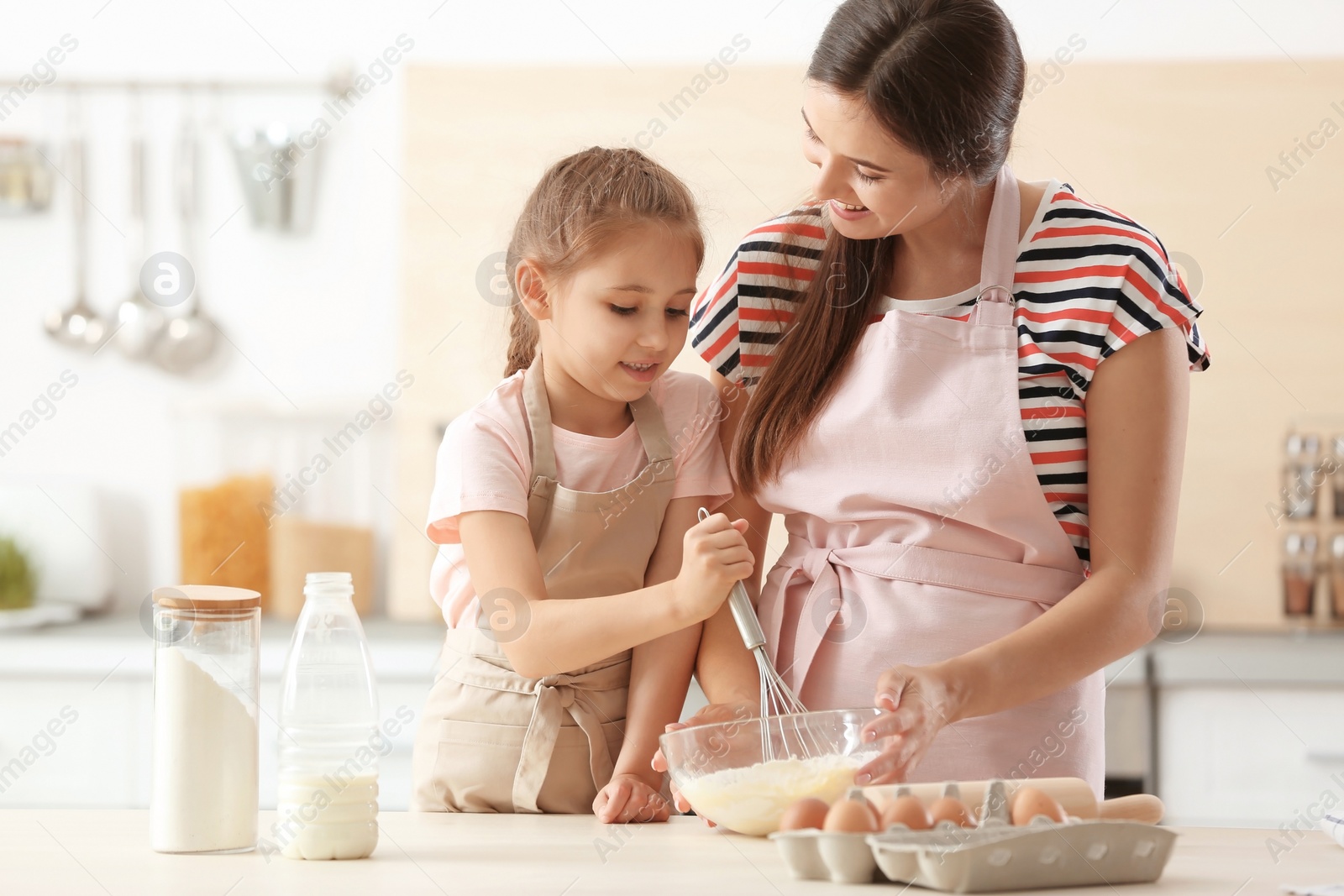 Photo of Mother and her daughter making dough at table in kitchen