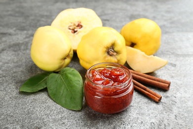 Photo of Delicious quince jam, fruits and cinnamon on grey table