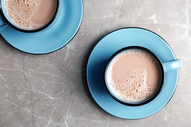 Cups with hot cocoa drink on grey table, top view