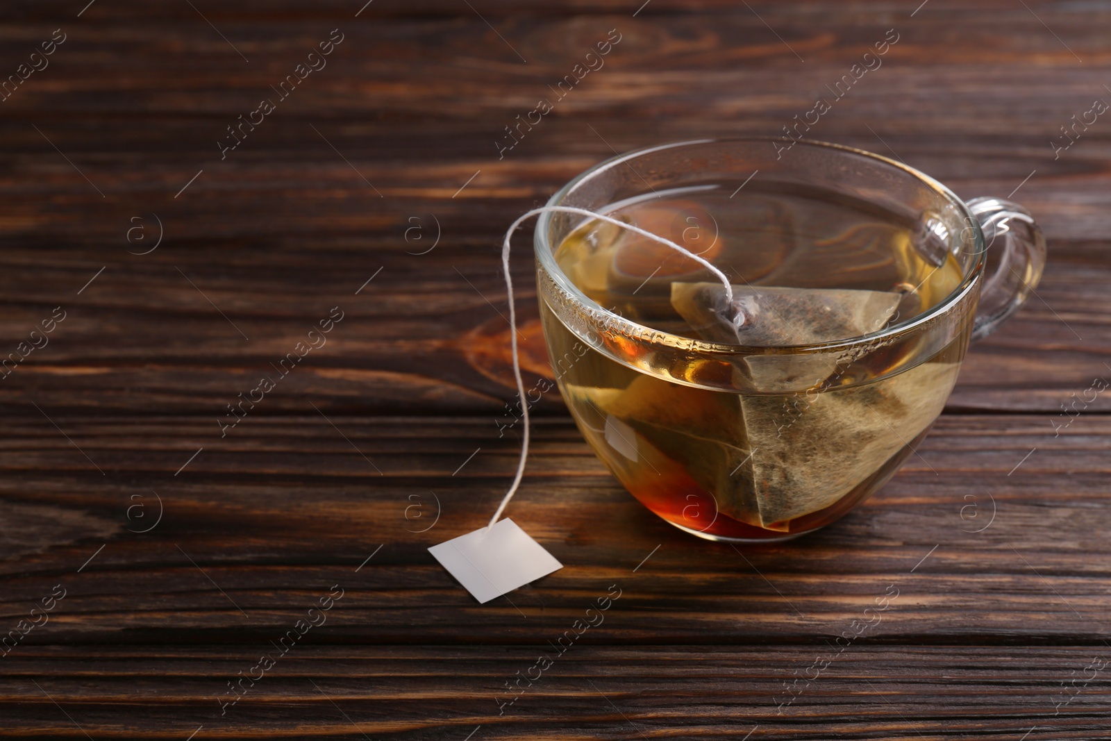 Photo of Tea bag in glass cup on wooden table. Space for text