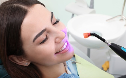 Photo of Woman undergoing teeth whitening procedure in clinic, closeup