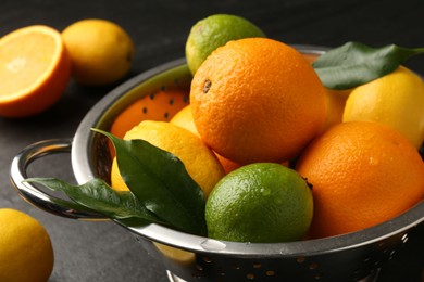 Fresh citrus fruits in colander on dark table, closeup