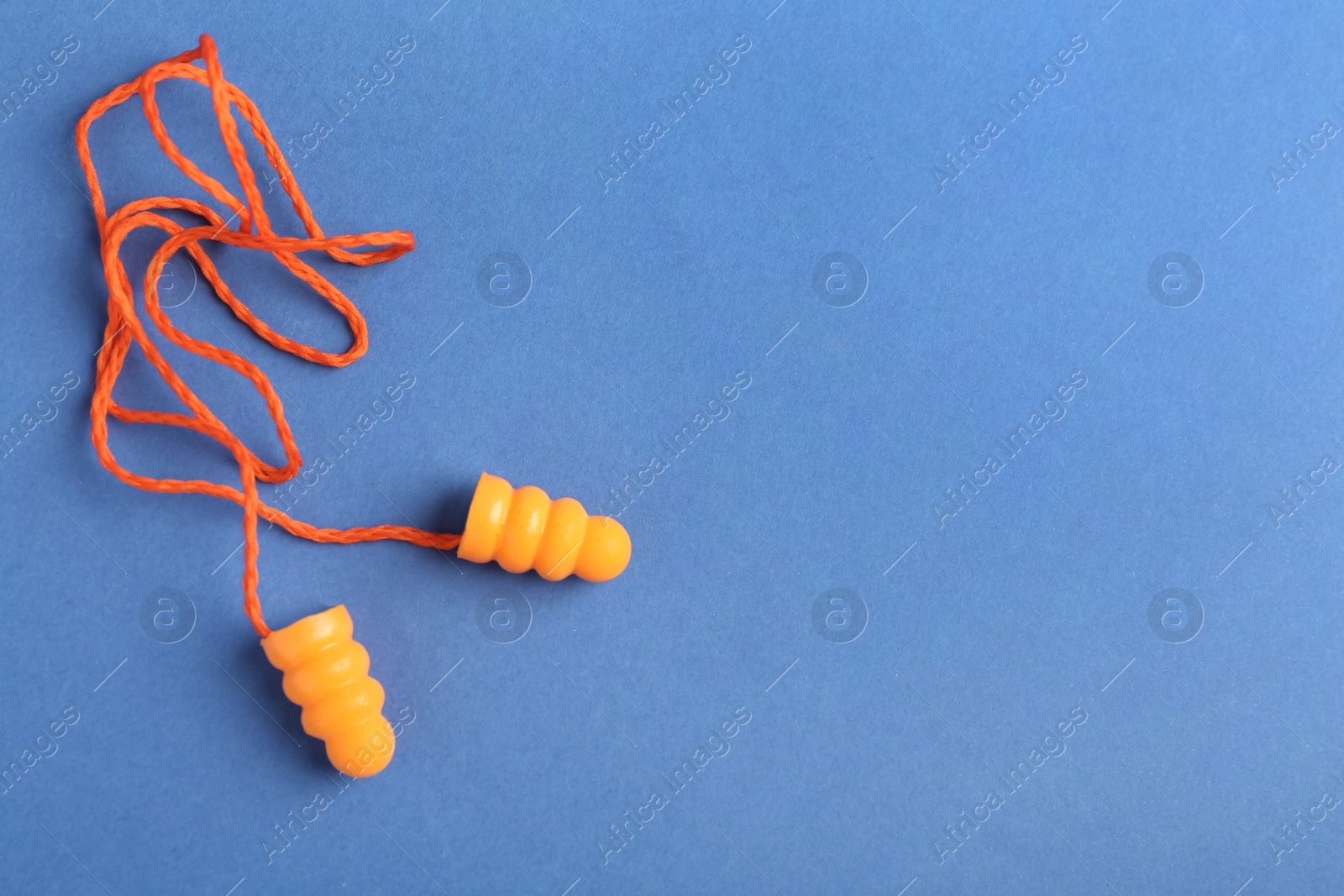 Photo of Pair of orange ear plugs with cord on blue background, top view. Space for text