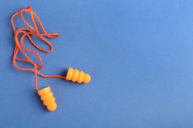 Pair of orange ear plugs with cord on blue background, top view. Space for text