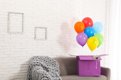 Gift box with bright air balloons on sofa against white brick wall. Space for text