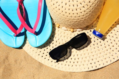 Photo of Straw hat, sunglasses, flip flops and refreshing drink on sand, above view. Beach accessories