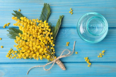 Beautiful mimosa flowers and glass vase on light blue wooden table, flat lay