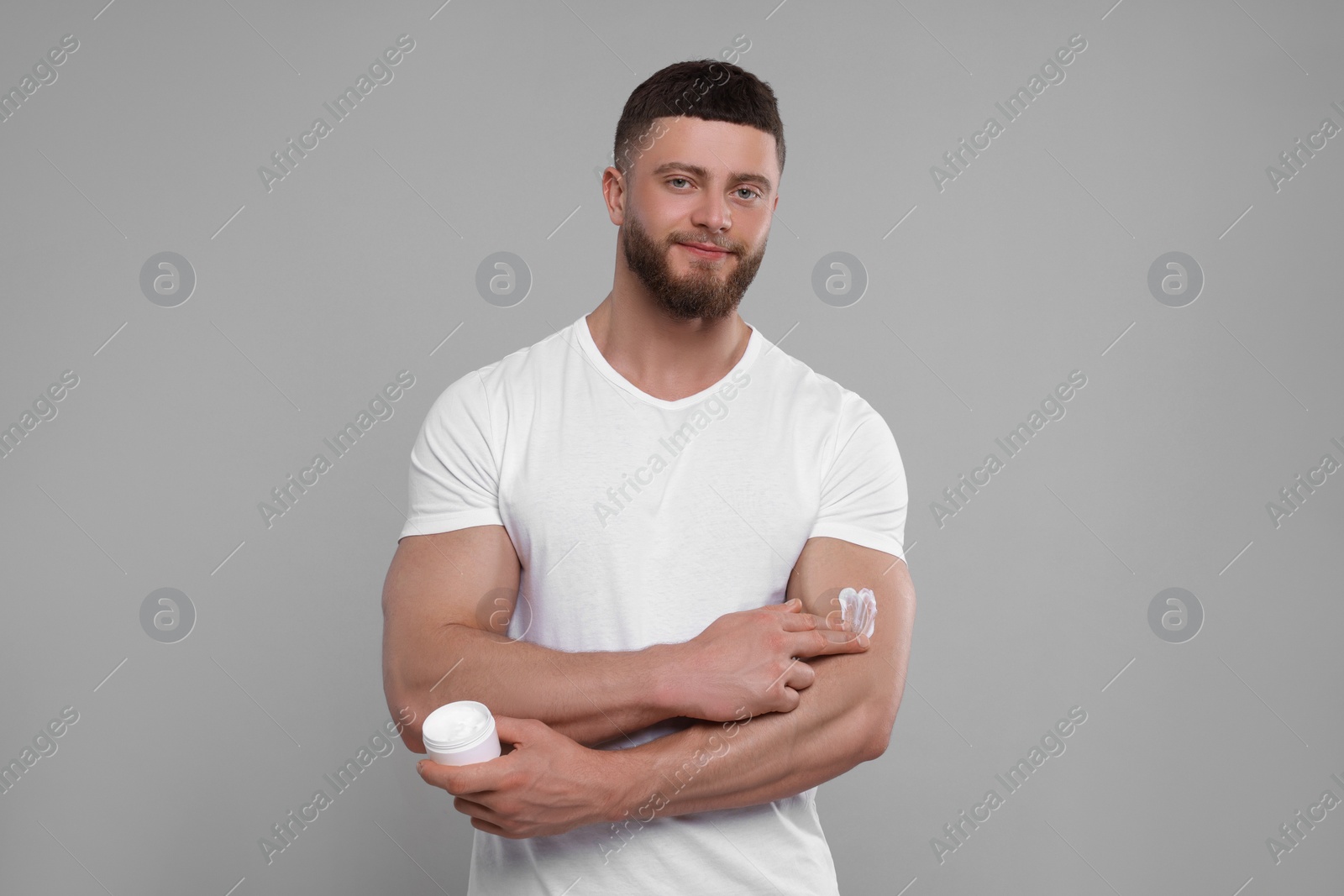 Photo of Handsome man applying body cream onto his arm on light grey background