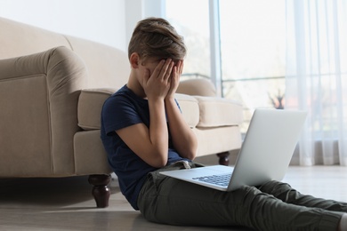 Photo of Frightened little child with laptop in room. Danger of internet