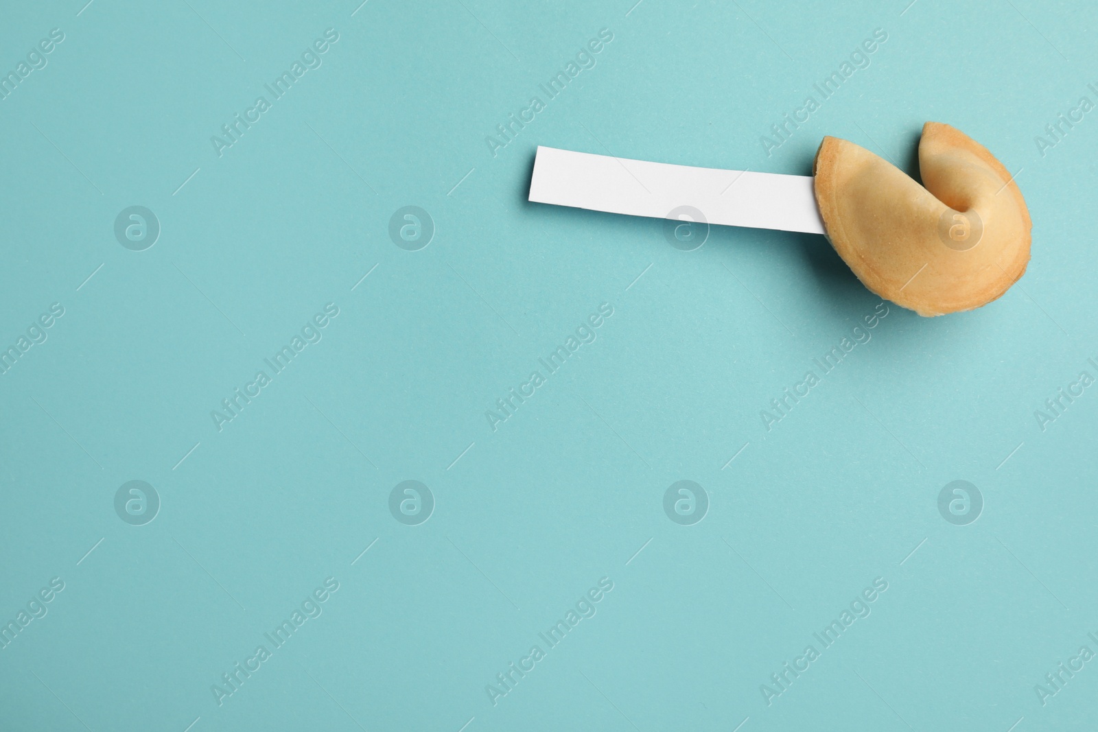 Photo of Tasty fortune cookie with prediction on light blue background, space for text