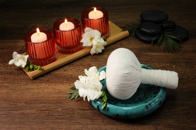 Photo of Herbal massage bag, burning candles and spa stones on wooden table