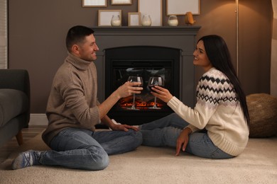 Photo of Lovely couple with glasses of wine spending time together near fireplace at home