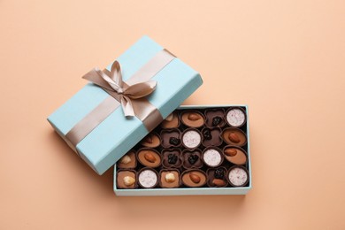 Photo of Open box of delicious chocolate candies on beige background, flat lay