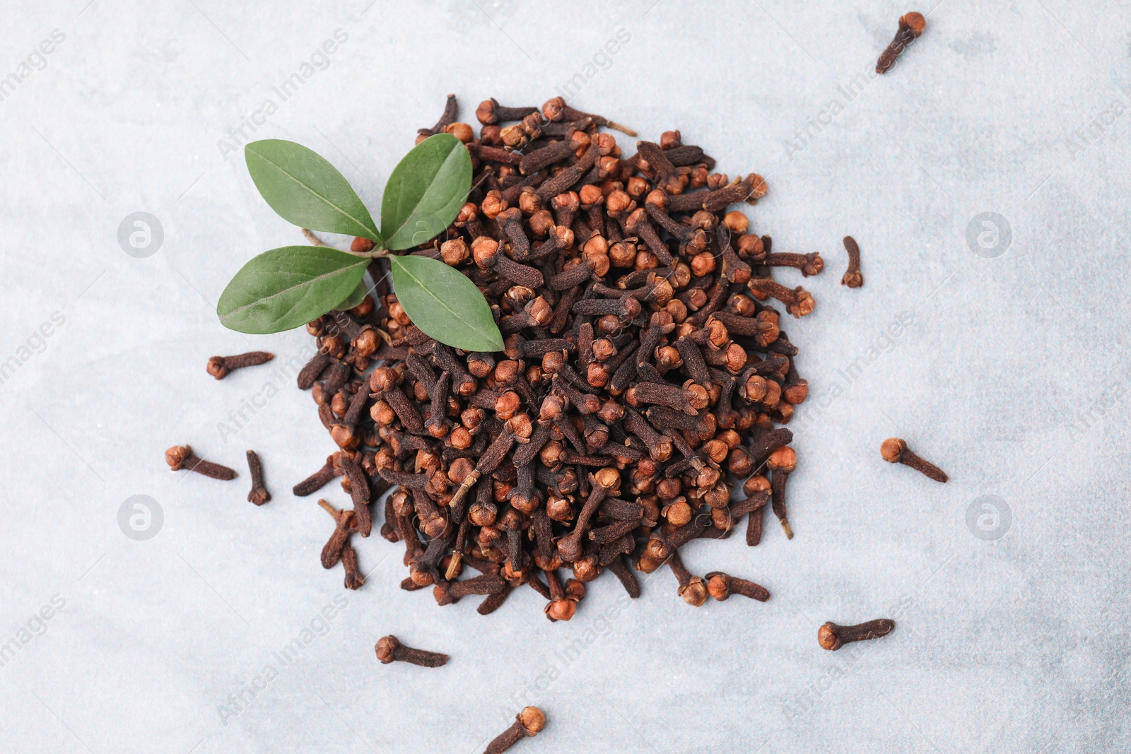 Photo of Pile of aromatic dried clove buds and leaves on grey table, top view