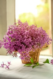 Photo of Beautiful lilac flowers in wicker basket on window sill indoors