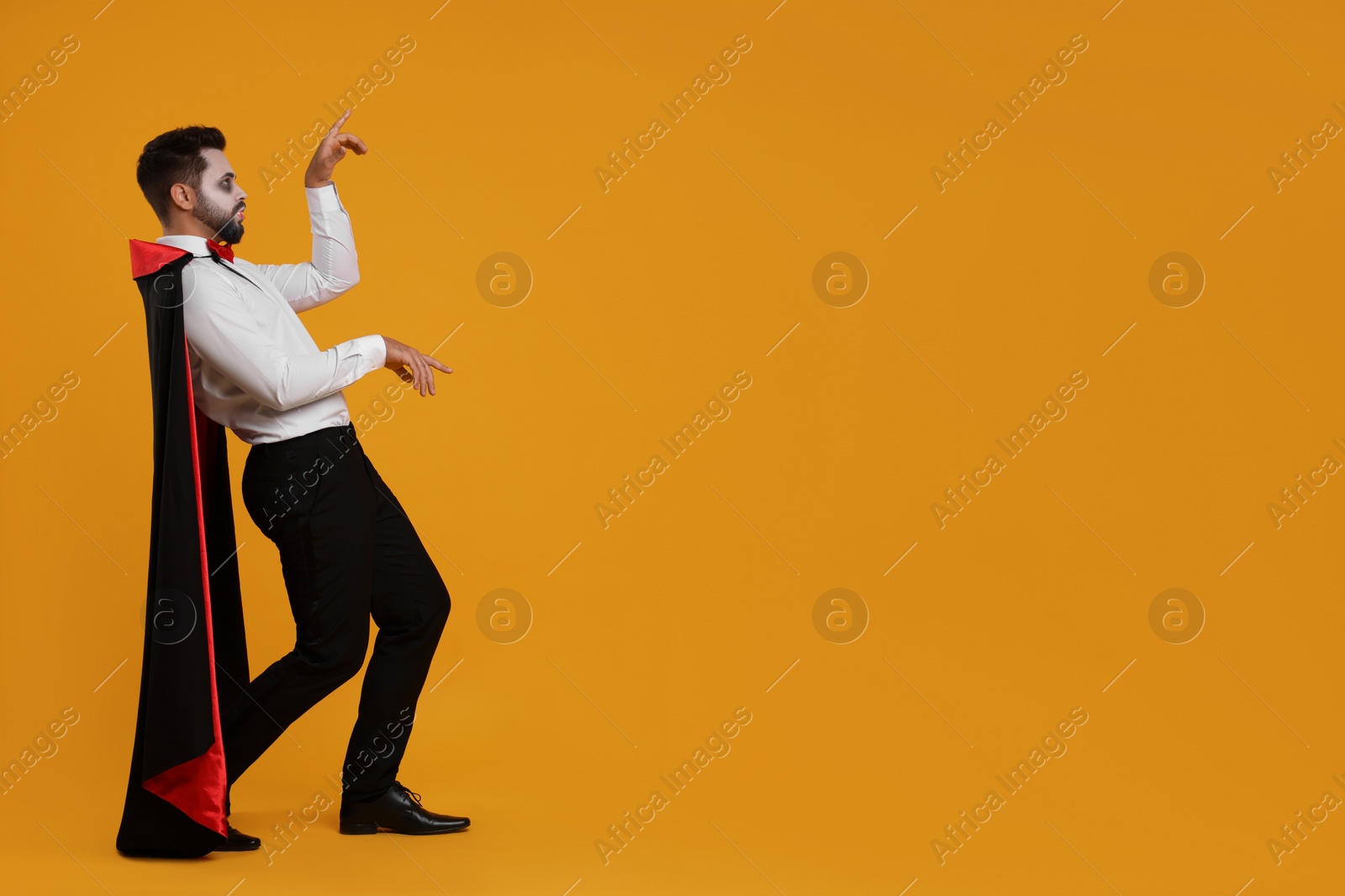 Photo of Man in scary vampire costume with fangs posing on orange background, space for text. Halloween celebration