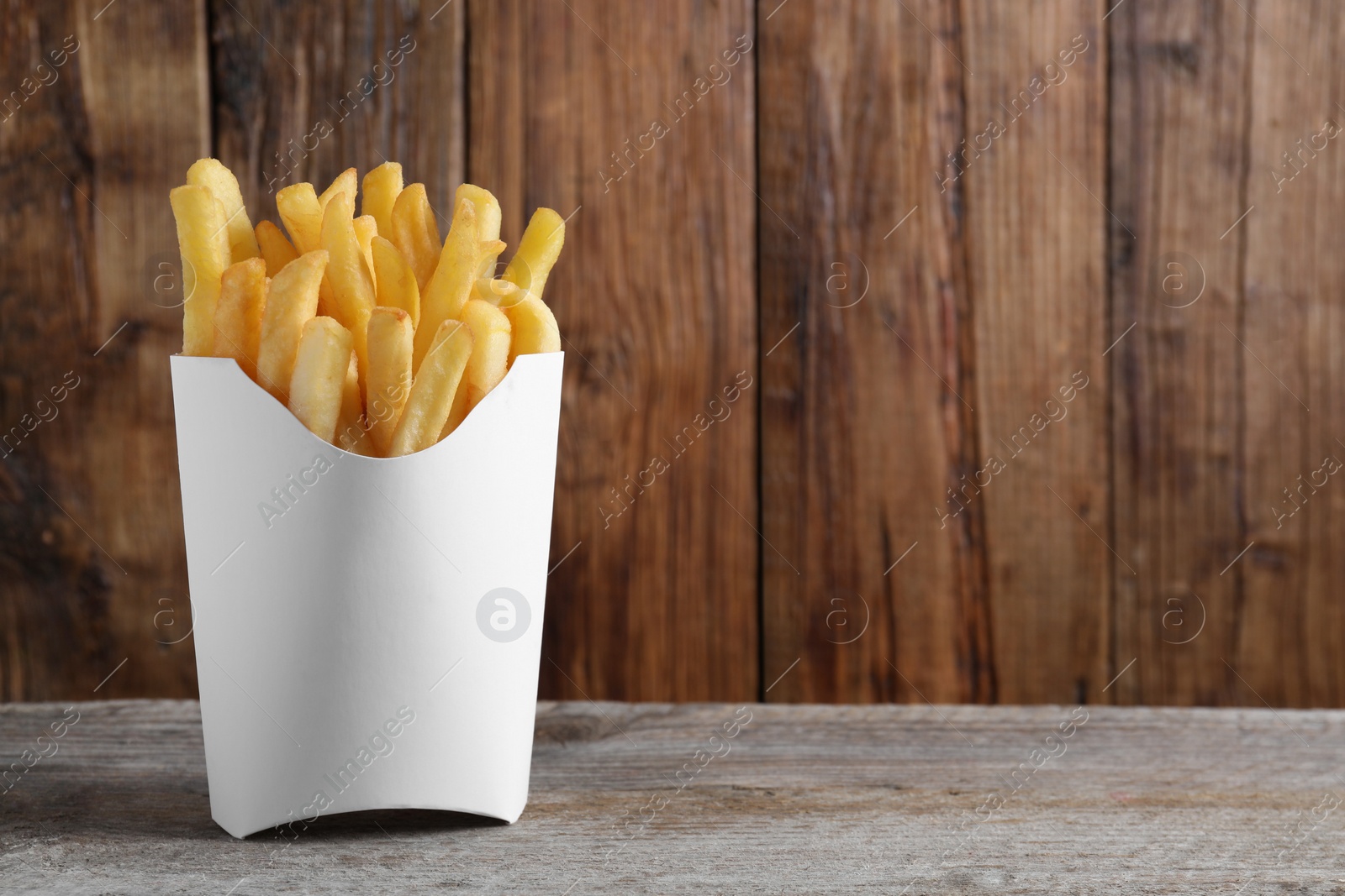 Photo of Delicious french fries in paper box on wooden table, space for text