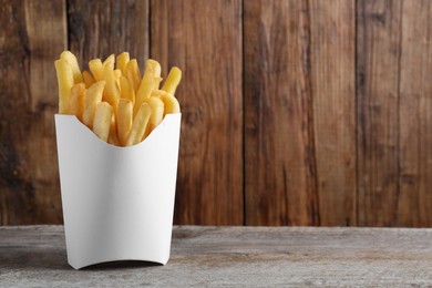 Delicious french fries in paper box on wooden table, space for text