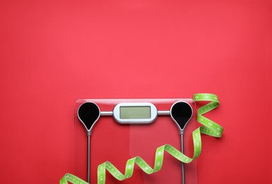 Photo of Electronic scales and measuring tape on red background, top view. Space for text