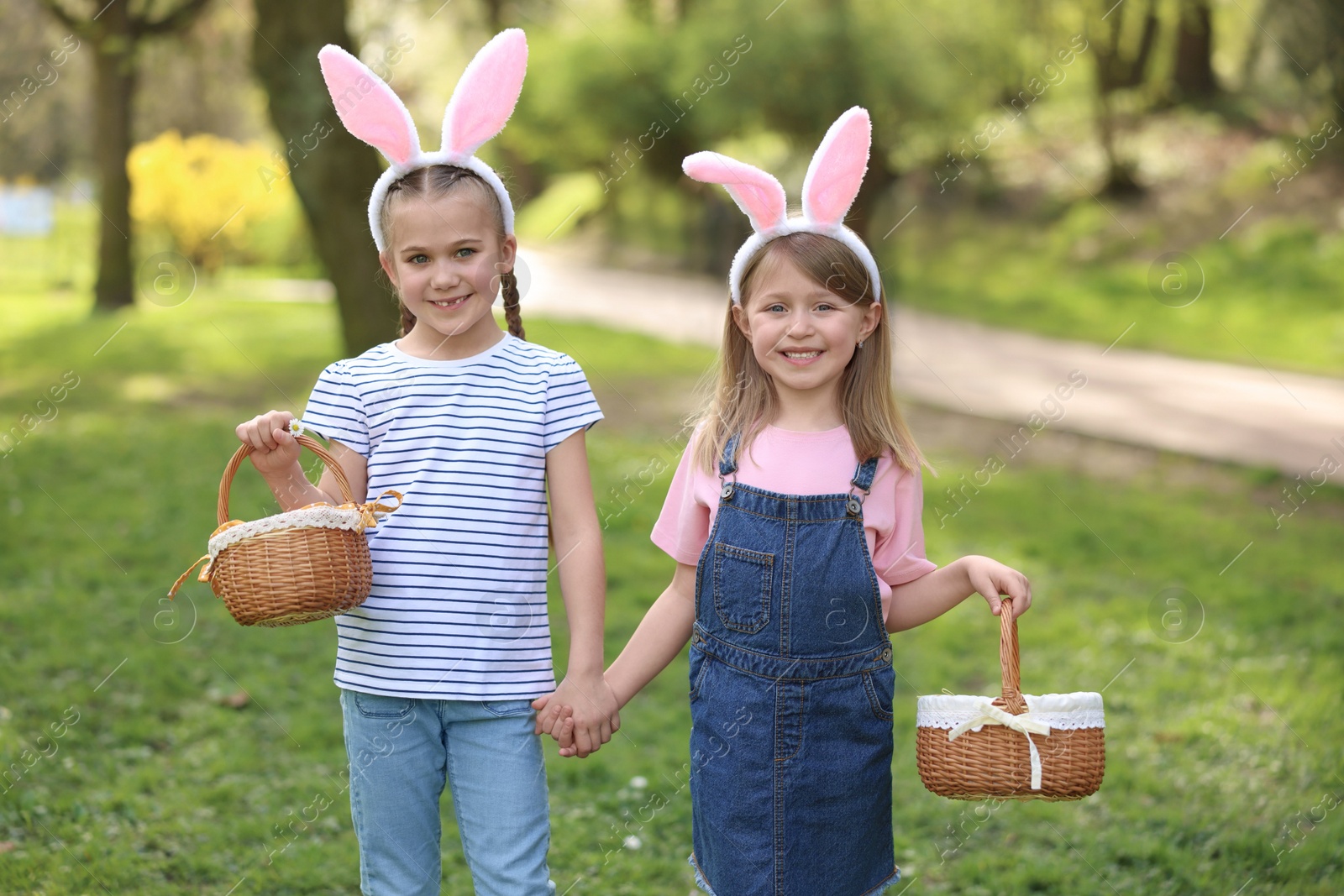 Photo of Easter celebration. Cute little girls with bunny ears holding wicker baskets outdoors