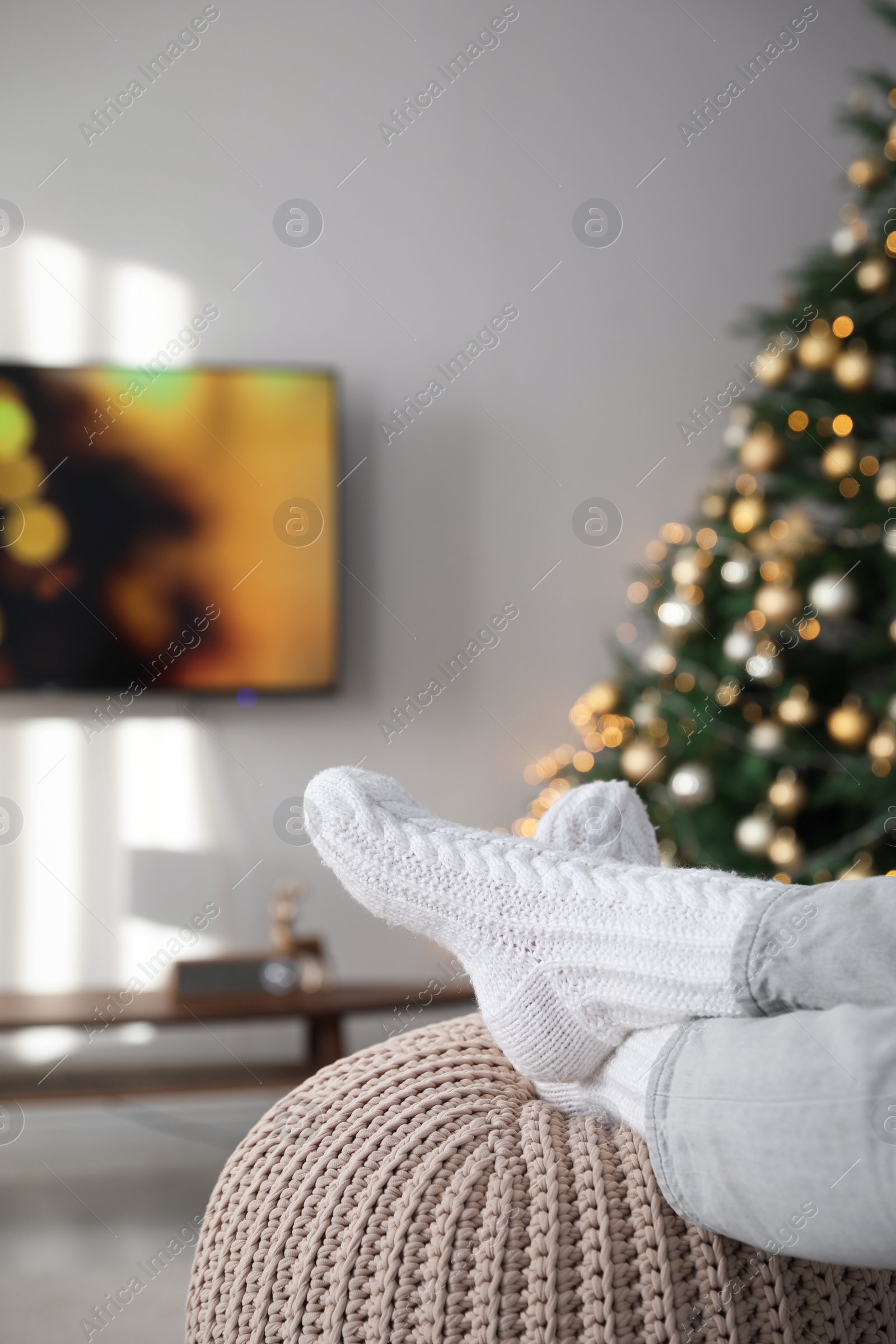 Photo of Woman wearing knitted socks in room decorated for Christmas, closeup