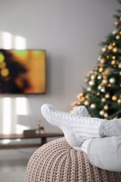 Photo of Woman wearing knitted socks in room decorated for Christmas, closeup