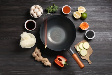 Photo of Empty iron wok and chopsticks surrounded by ingredients on dark grey wooden table, flat lay