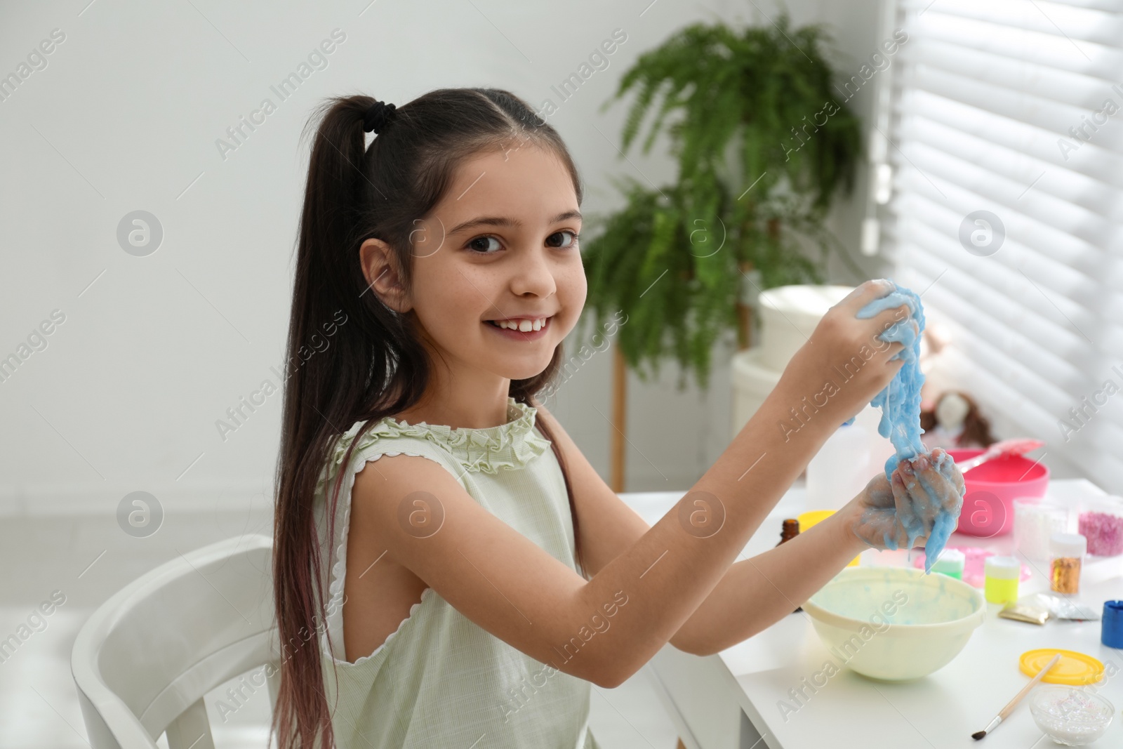 Photo of Cute little girl making DIY slime toy at table in room