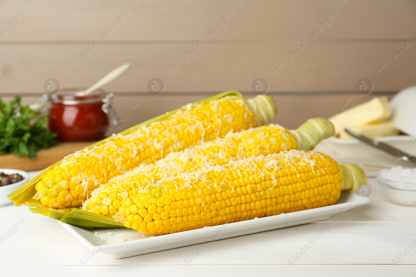 Photo of Plate with tasty cooked corn cobs on white wooden table, closeup