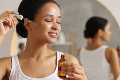 Photo of Smiling woman applying serum onto her face in bathroom