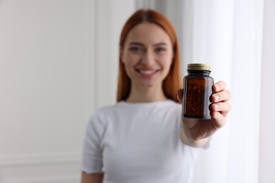 Beautiful young woman with jar of vitamin pills at home, selective focus