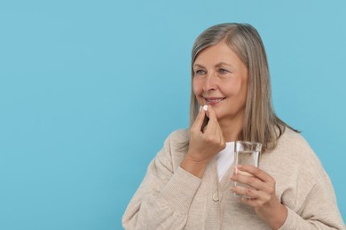 Photo of Senior woman with glass of water taking pill on light blue background. Space for text