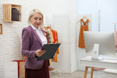 Female business owner with clipboard in boutique. Space for text