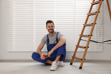 Photo of Worker in uniform and stepladder near horizontal window blinds indoors