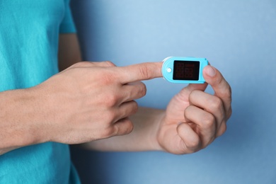 Photo of Young man checking pulse with blood pressure monitor on finger against color background, closeup