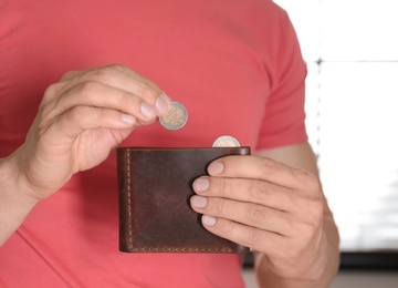 Man putting coin into wallet indoors, closeup