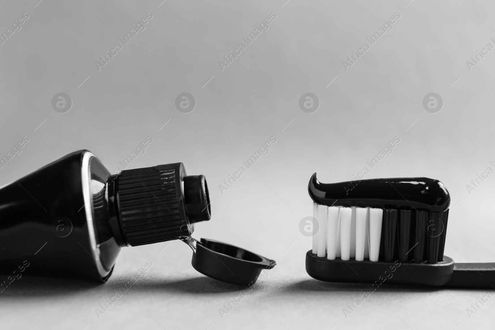 Photo of Brush and tube with charcoal toothpaste on light grey background, closeup. Space for text