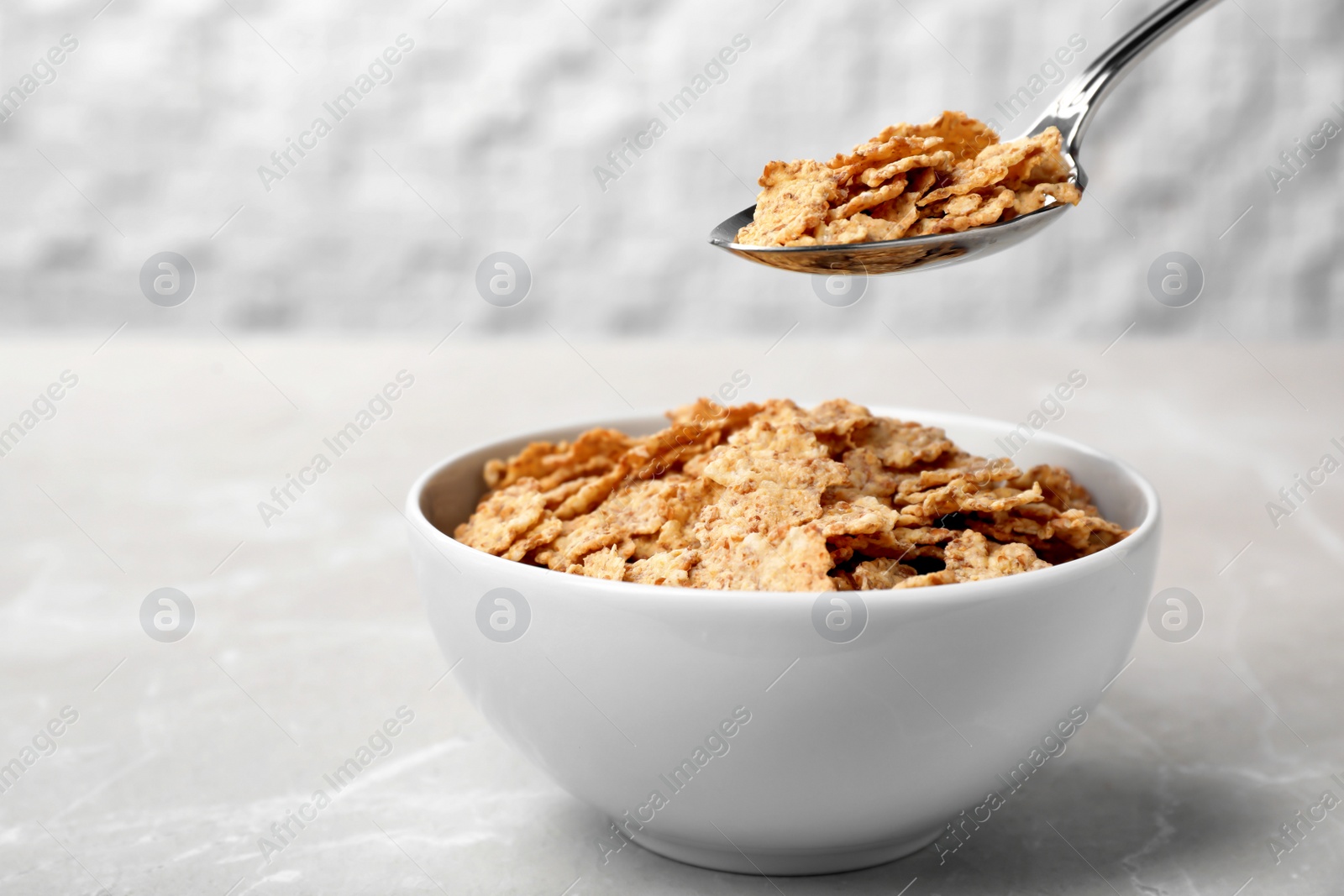 Photo of Spoon with cornflakes over bowl on table. Whole grain cereal