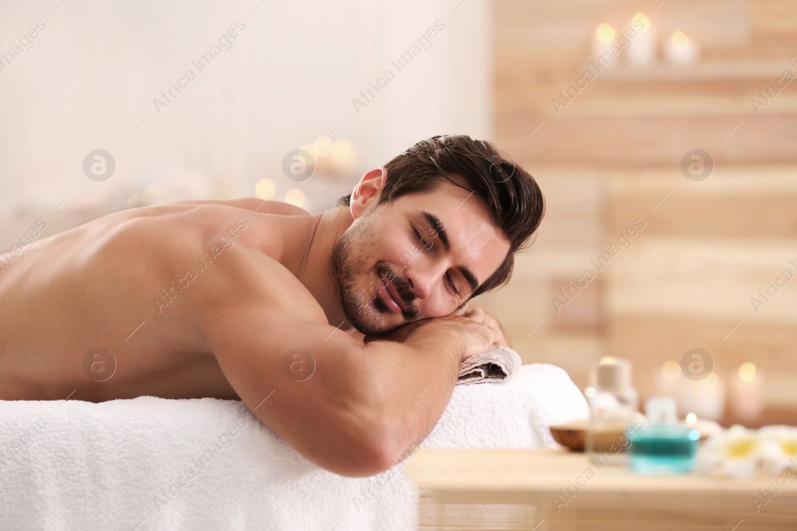 Photo of Handsome young man relaxing on massage table in spa salon, space for text