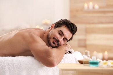 Photo of Handsome young man relaxing on massage table in spa salon, space for text